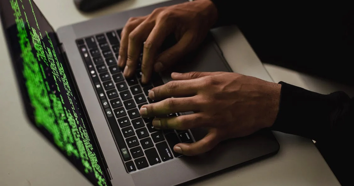 two hands coding on a laptop with green text on the black laptop screen