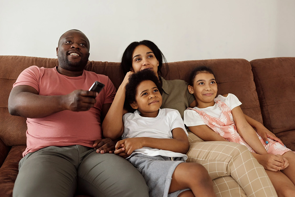 a family sitting on the couch together with the dad holding a tv remote