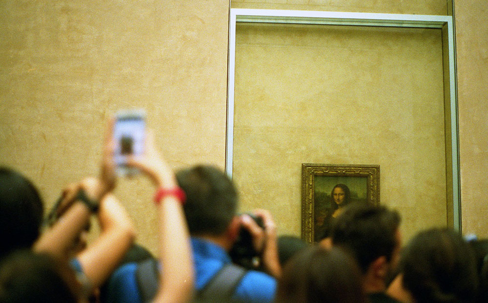 a crowd of people standing in front of the mona lisa in the louvre, some of which are taking photos