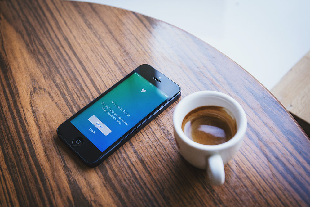 a phone open to twitter on a table next to a mug of coffee