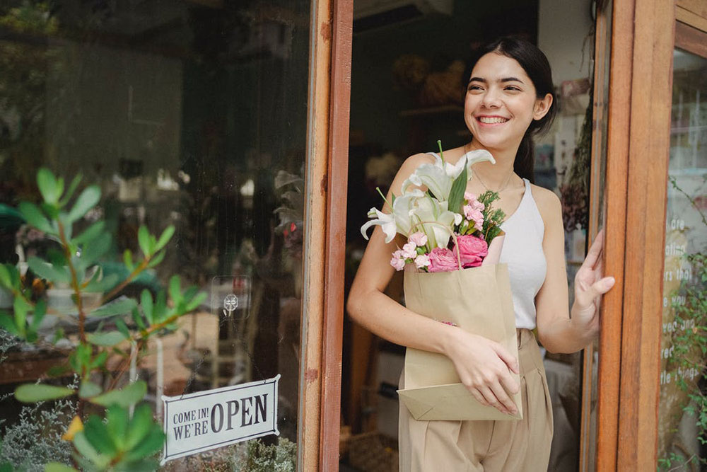 a woman holding a bag with a small flower bouquet inside as she leaves a store