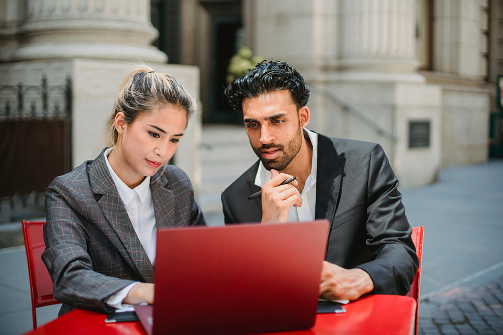 woman and man sitting outside somewhere looking at a laptop together