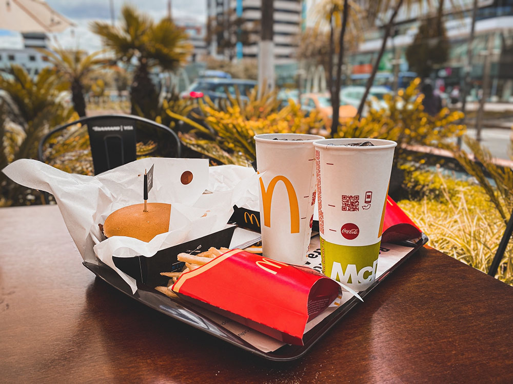 mcdonalds meal consisting of a burger fries and two drinks on a tray on a table outside