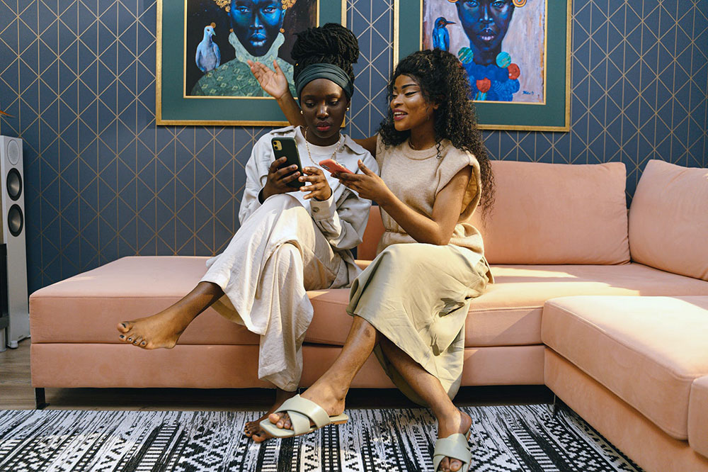 two women sitting on a couch, showing each other what's on their phones