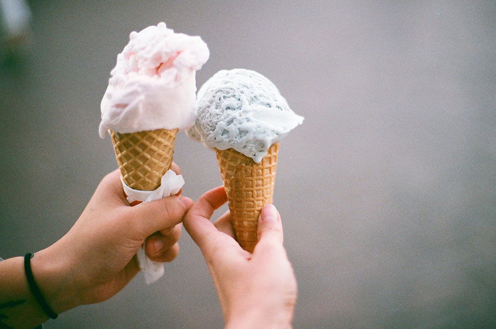 two people's hands, each holding an ice cream cone