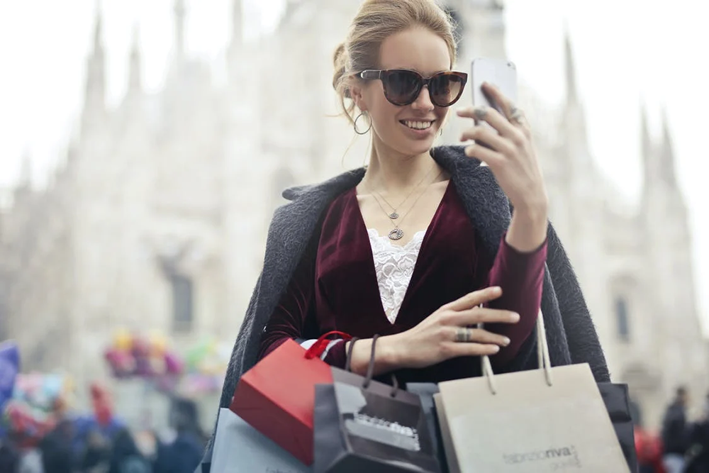 a woman holding multiple shopping bags while wearing sunglasses and looking at her phone