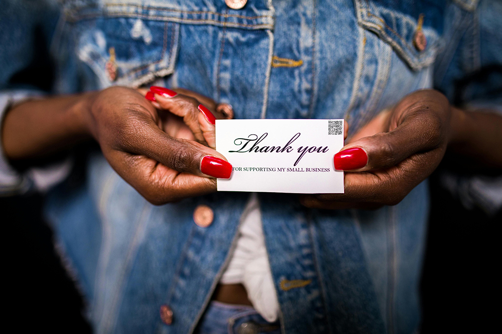 a woman holding a thank you for supporting my small business card with an audio qr code in the top right corner