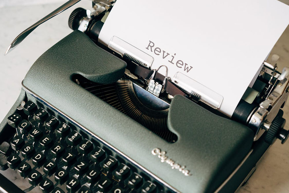 black and white typewriter on table with a piece of paper sticking out that says review